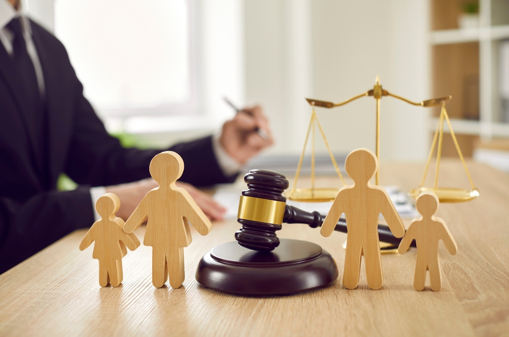 Gavel, sound block and little wooden figures of parents and children placed on desk in courthouse up close